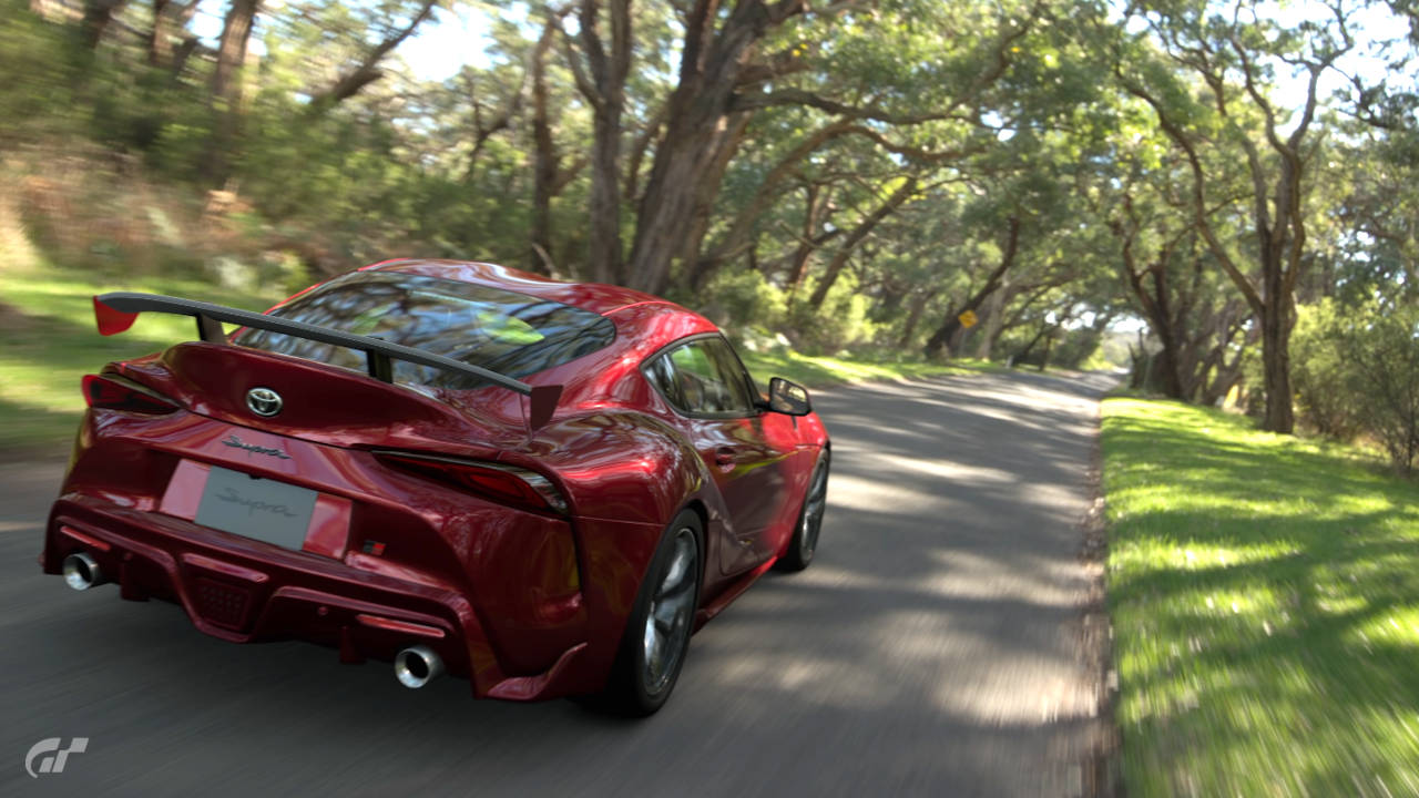 Gran Turismo 7 - czerwone auto jedzie przez drogę wśród drzew - screen zrobiony w trybie fotograficznym