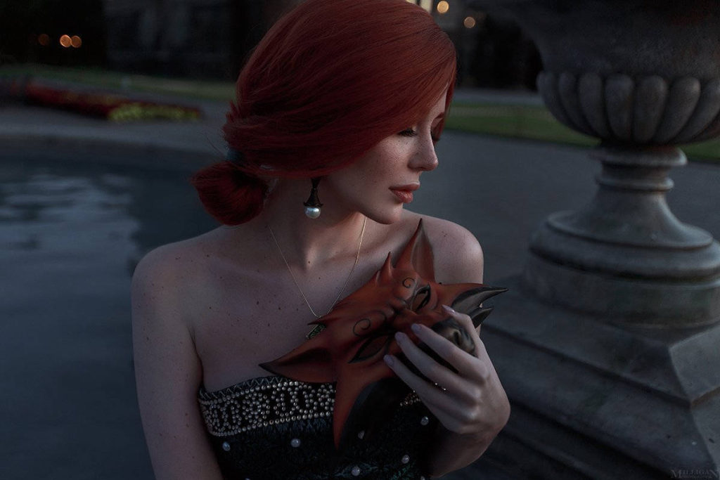 cosplay - Triss - Vick_Torie jako Triss siedzi na murku fontanny i przyciska do siebie maskę lisa